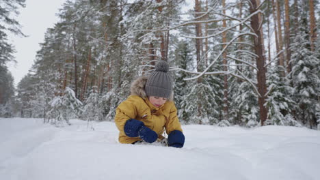 A-boy-in-a-yellow-jacket-takes-out-a-blade-of-grass-and-examines-studying-the-winter-forest-winter-walks-and-through-the-snowy-forest-in-slow-motion.-The-concept-of-a-free-environment-for-children